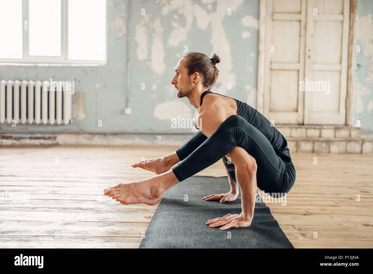 Yoga maschio in classe, l'equilibrio di formazione. Esercizio sul tappeto in palestra con grunge interni. Montare l'allenamento al chiuso Foto Stock