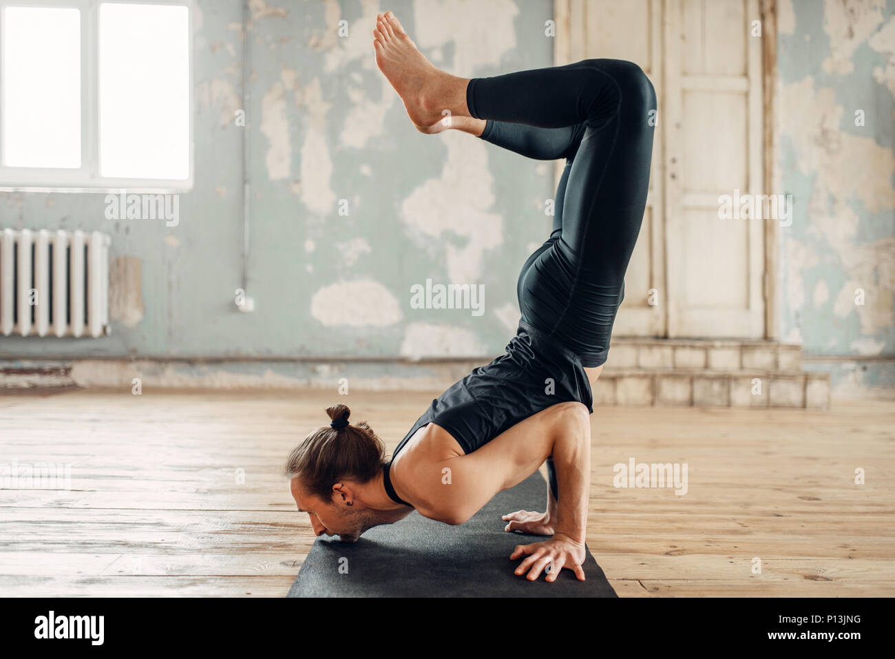 Maschio di yoga in palestra, esercizio di bilanciamento su mat. Allenamento fitness in ambienti chiusi. Uno stile di vita sano Foto Stock
