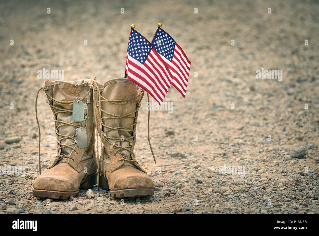 Il vecchio militare stivali da combattimento con dog tag e due piccole bandierine americane. Ghiaia rocciosa sfondo con copia spazio. Il Memorial Day o giorno dei veterani del concetto. Foto Stock