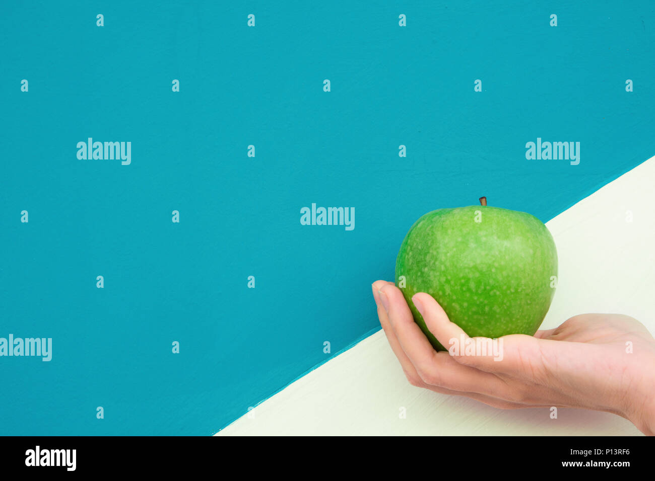 Giovane donna caucasica tiene in mano organico verde di Apple sulla bicromia bianco sfondo turchese. Vitamine Dieta sana Estate Detox Superfoods vegano con Foto Stock