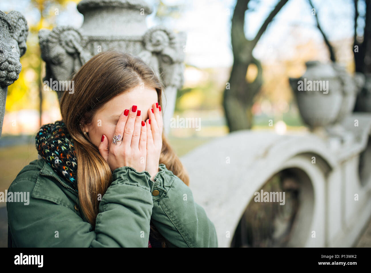 Giovane donna attraente con unghie rosse che copre il volto con le mani Foto Stock