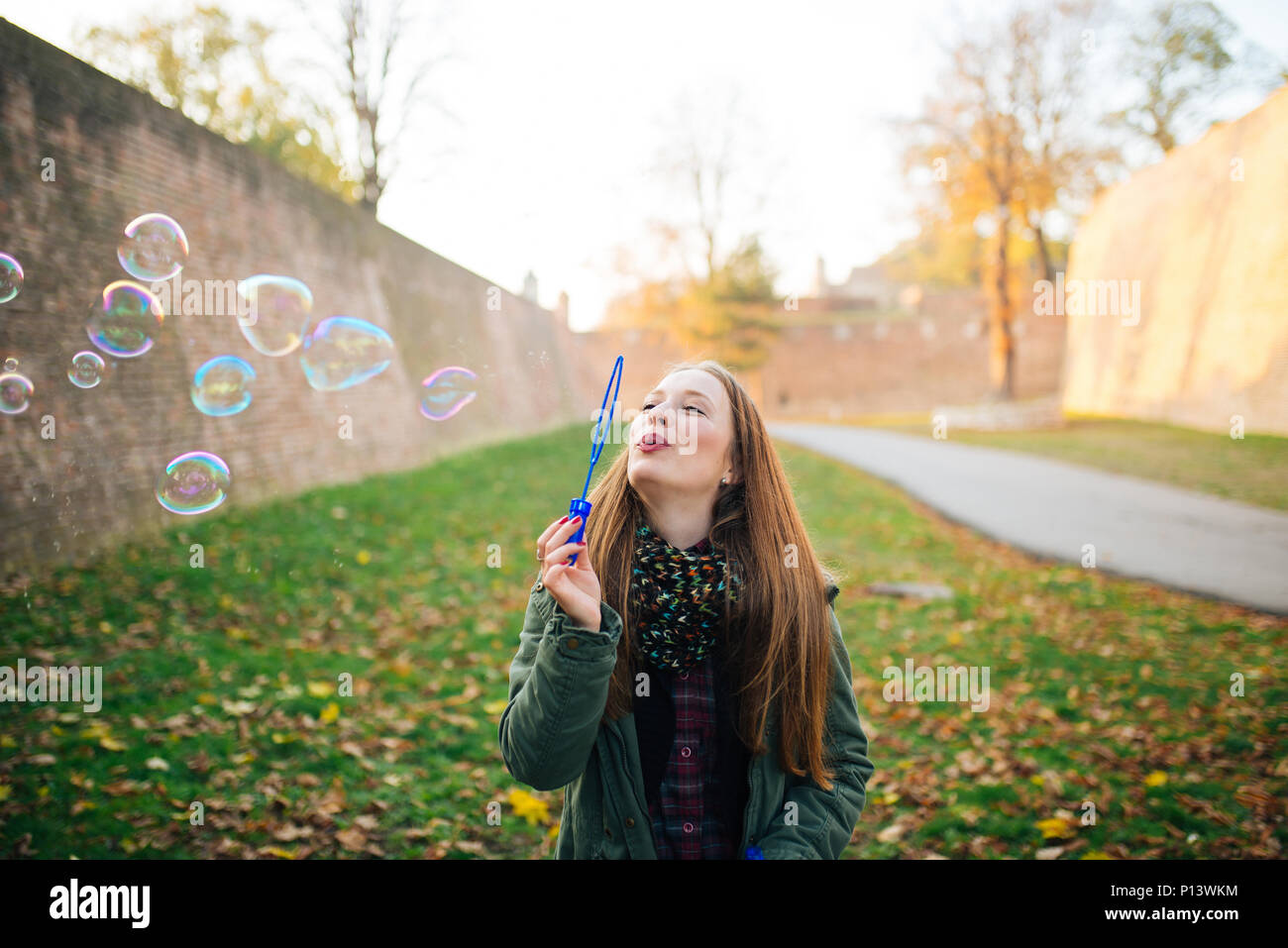 Attraente giovane donna sta godendo di rendere un bolle nel parco pubblico. Suolo coperto di foglie di autunno. Foto Stock