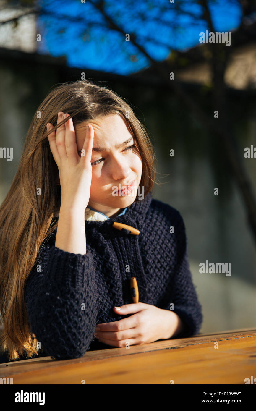 Un triste e depresso carino bambina seduti all'aperto al tavolo. La solitudine e la depressione del concetto. Foto Stock