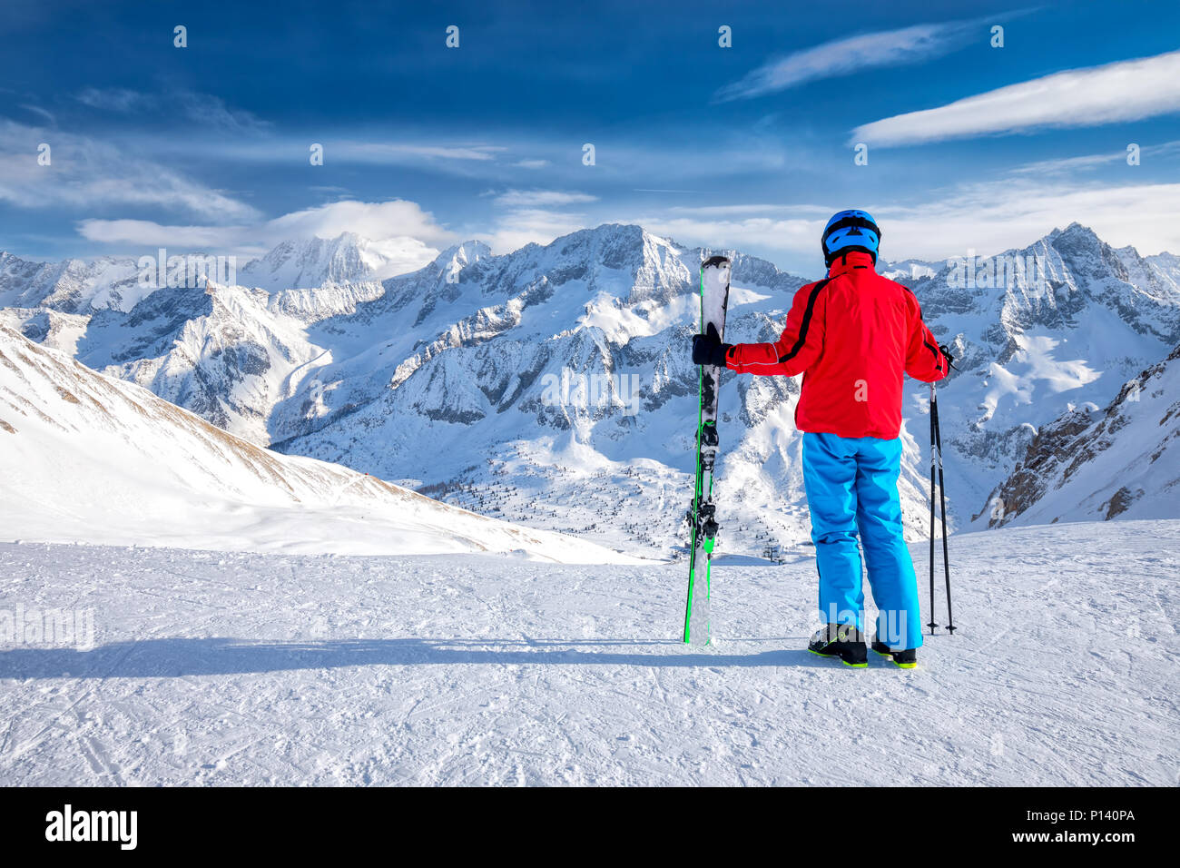 Giovane sciatore felice seduto sulla cima delle montagne e godersi la vista delle Alpi Retiche, Passo Tonale, Italia, Europa. Foto Stock