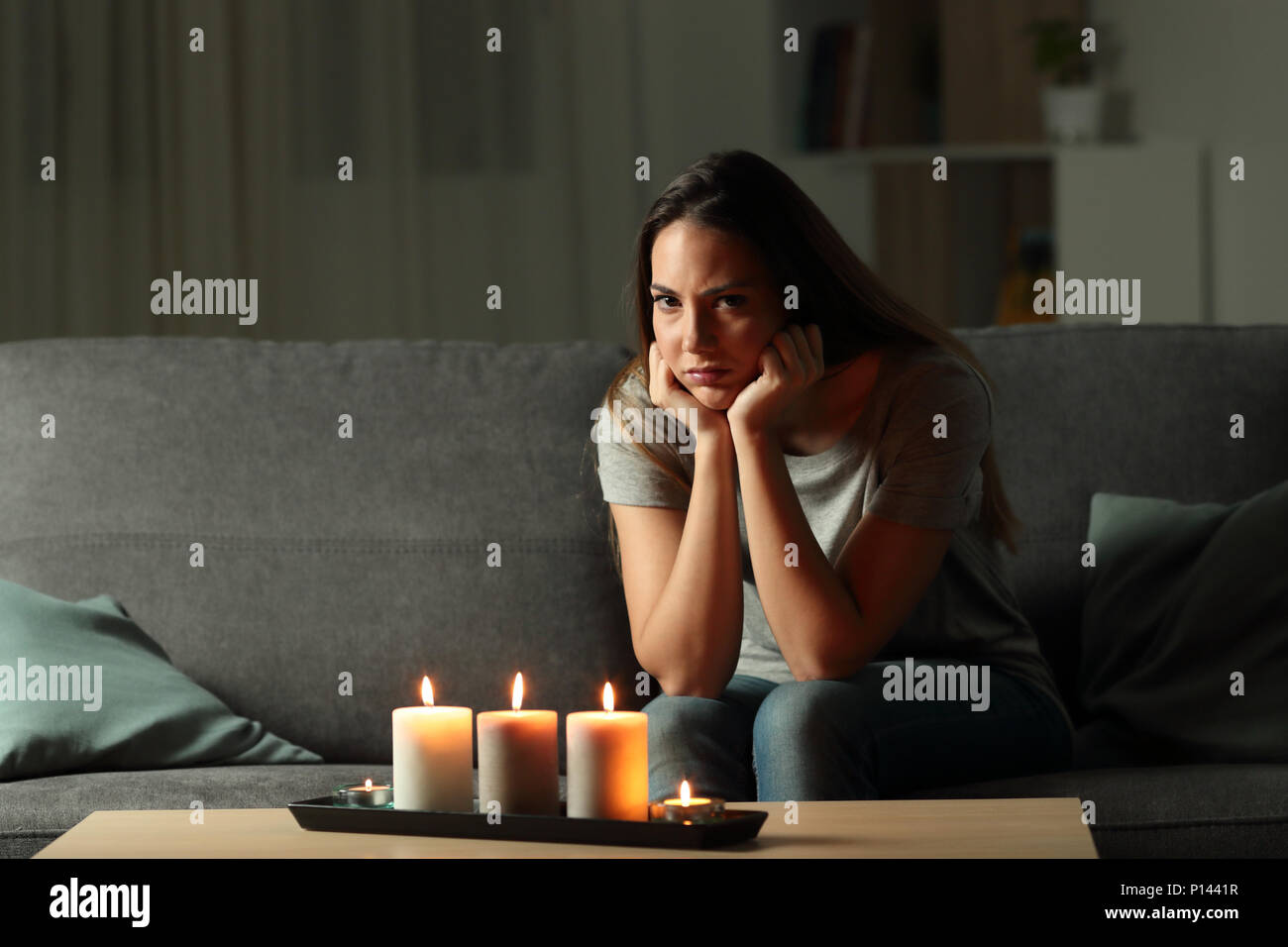 Arrabbiato donna che guarda la fotocamera durante un blakout seduta su un divano nel salotto di casa Foto Stock