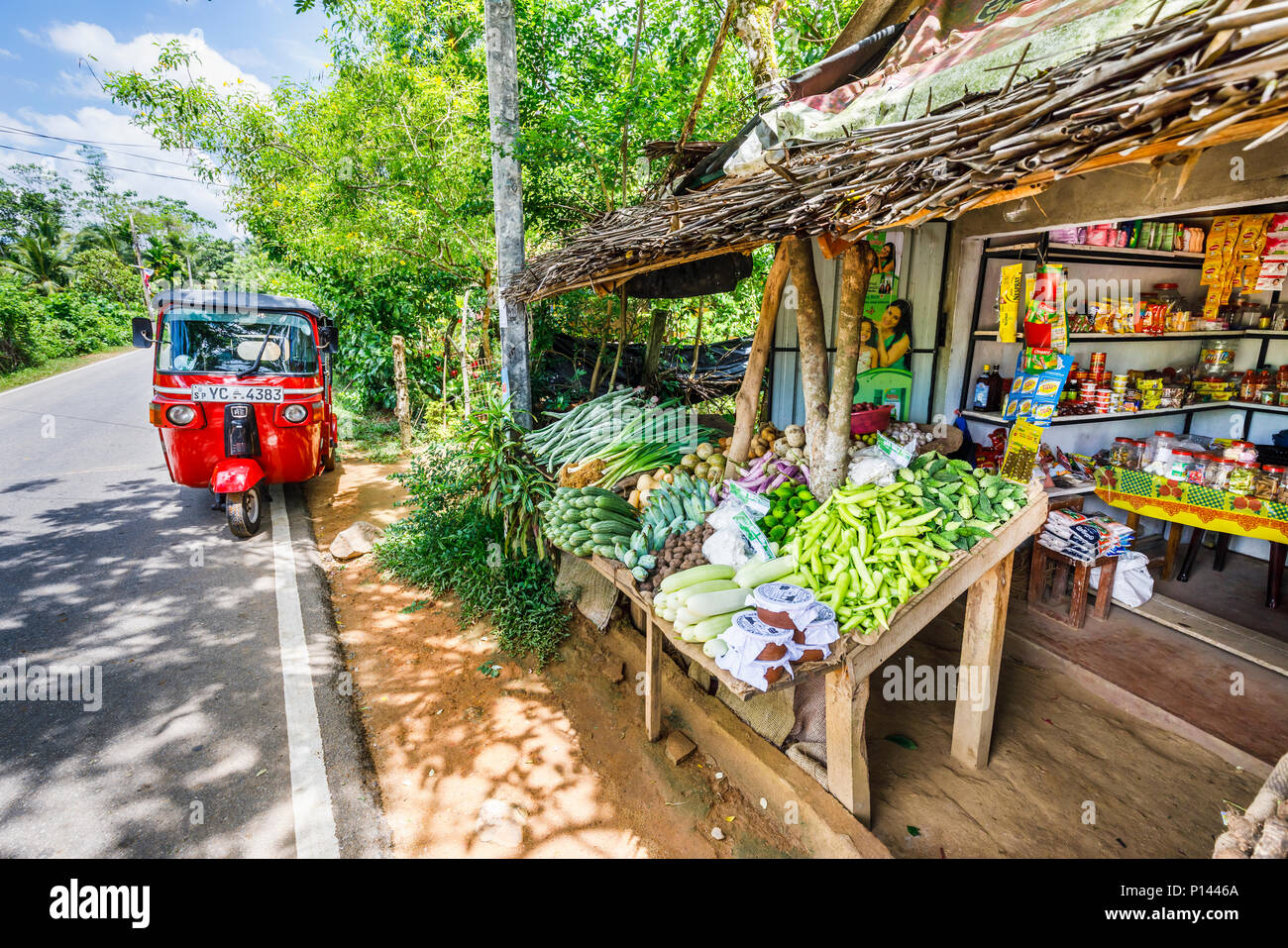Rosso di tuk-tuk parcheggiato in strada al di fuori di una strada rurale di vegetali e di stallo di generi alimentari con prodotti locali, Horagampita distretto, vicino a Galle, Sri Lanka Foto Stock