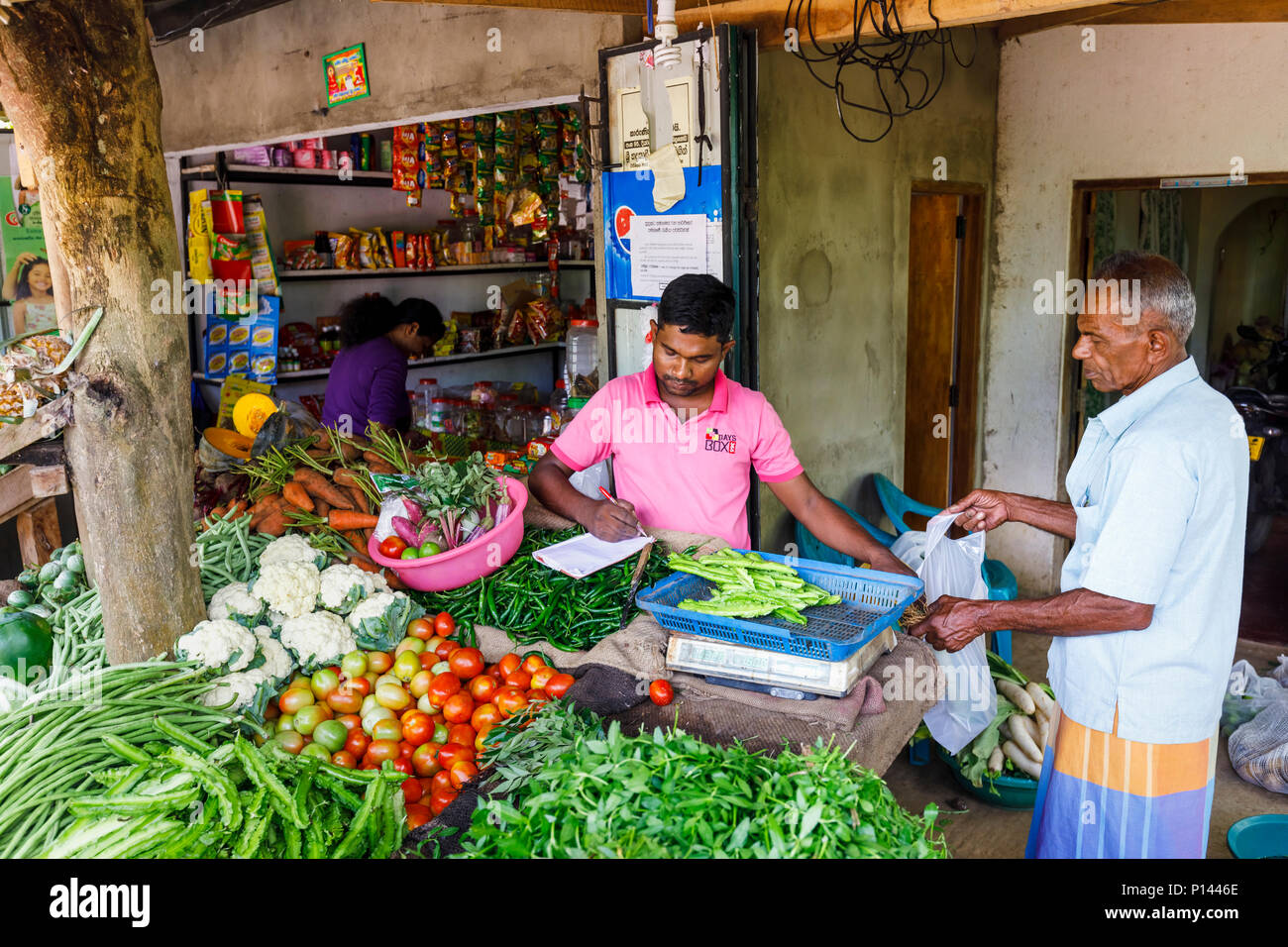 Stallholder in una strada rurale di vegetali e negozio di generi alimentari bancarella vendendo prodotti freschi per un uomo locale, Horagampita distretto, vicino a Galle, Sri Lanka Foto Stock