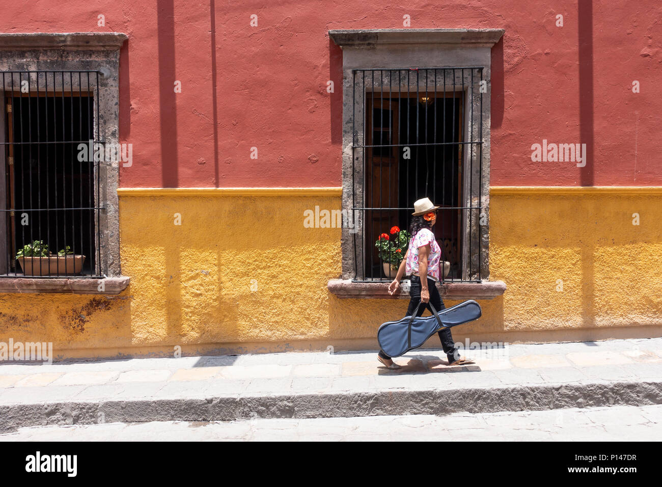 Una donna messicana a camminare su una strada di San Miguel De Allende portando un caso di chitarra Foto Stock