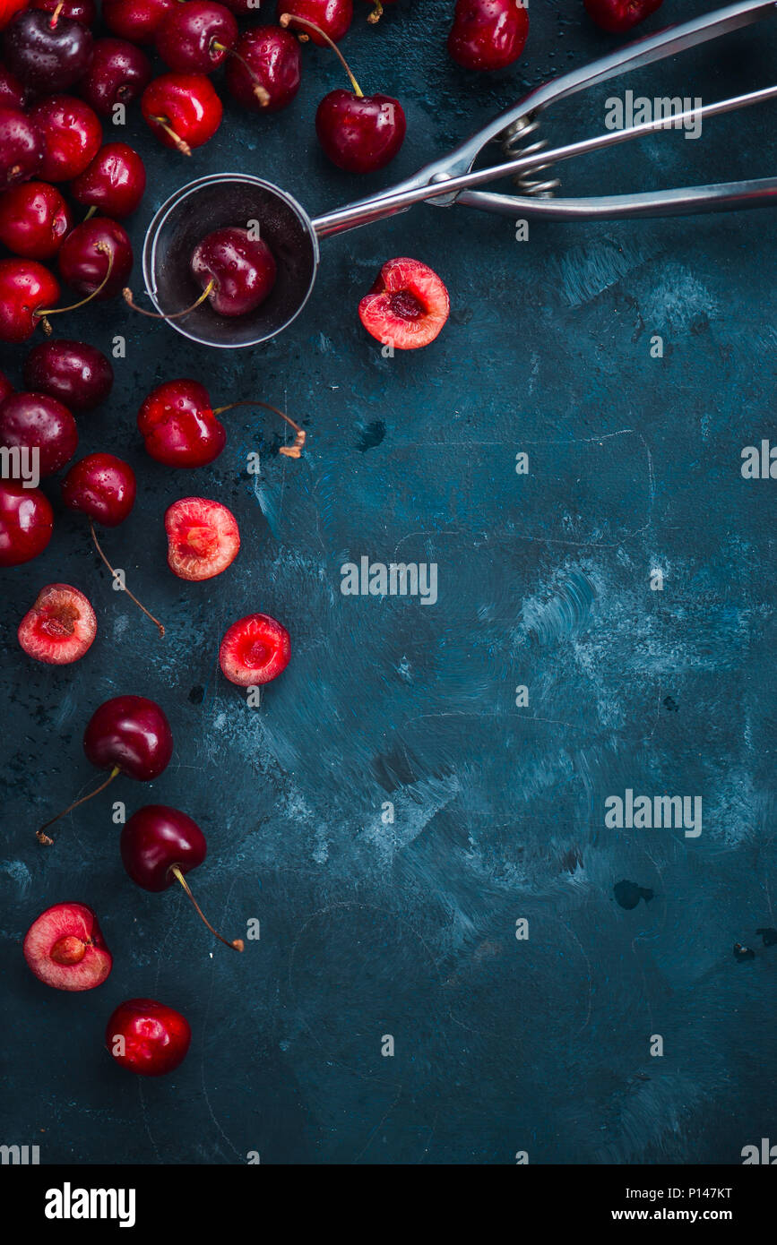 Le ciliegie e gelato cucchiaio su un cemento grigio Sfondo, estate bacche concetto con copia spazio. Rendendo piatto da dessert lay in folle i toni di colore Foto Stock