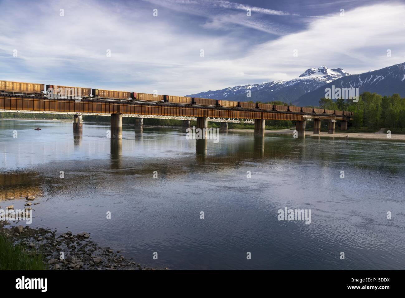 Treno merci Canadian Pacific Railway che attraversa la Columbia River Bank Water Revelstoke BC Canada. Panoramica panoramica delle Montagne Rocciose di Selkirk con vista panoramica sullo skyline Foto Stock