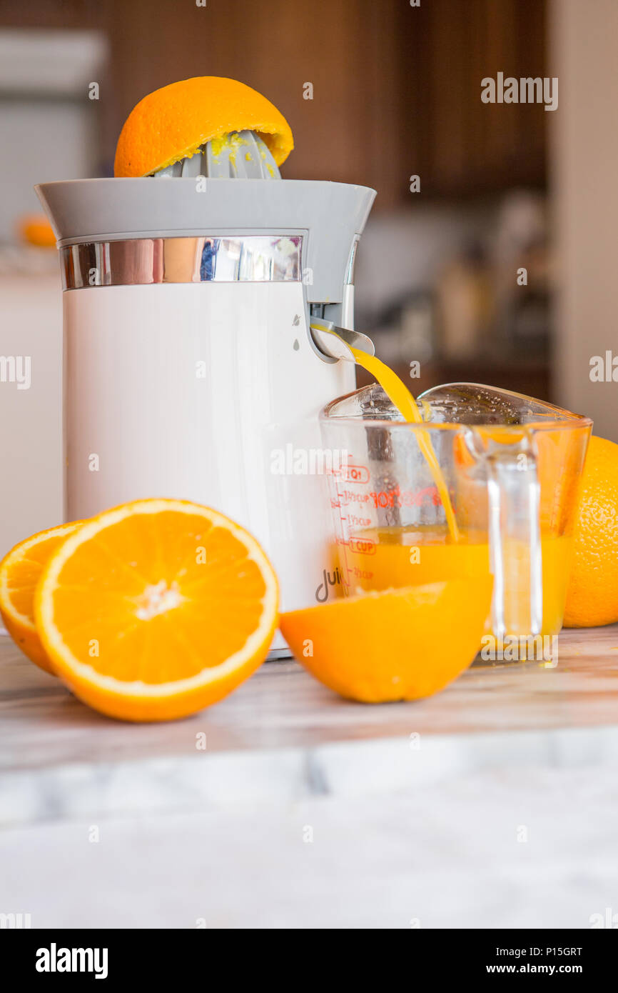 Il piano portapaziente arancione elettrico e spremitura di agrumi in una cucina domestica con fresco intero e tagliare le arance . Foto Stock
