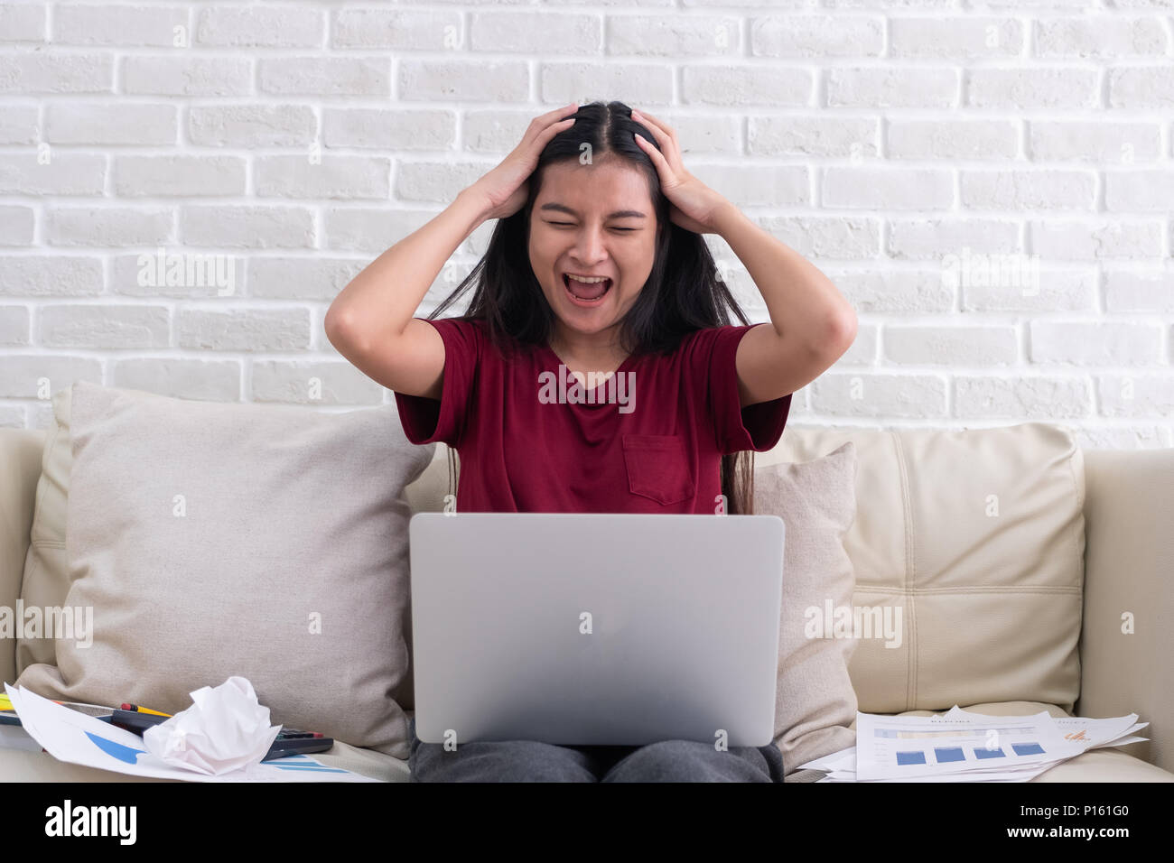 Donna asiatica freelancer gridare con stress emozione mentre si lavora con il computer portatile e documenti cartacei al divano nel soggiorno in casa.Il lavoro a casa concept Foto Stock