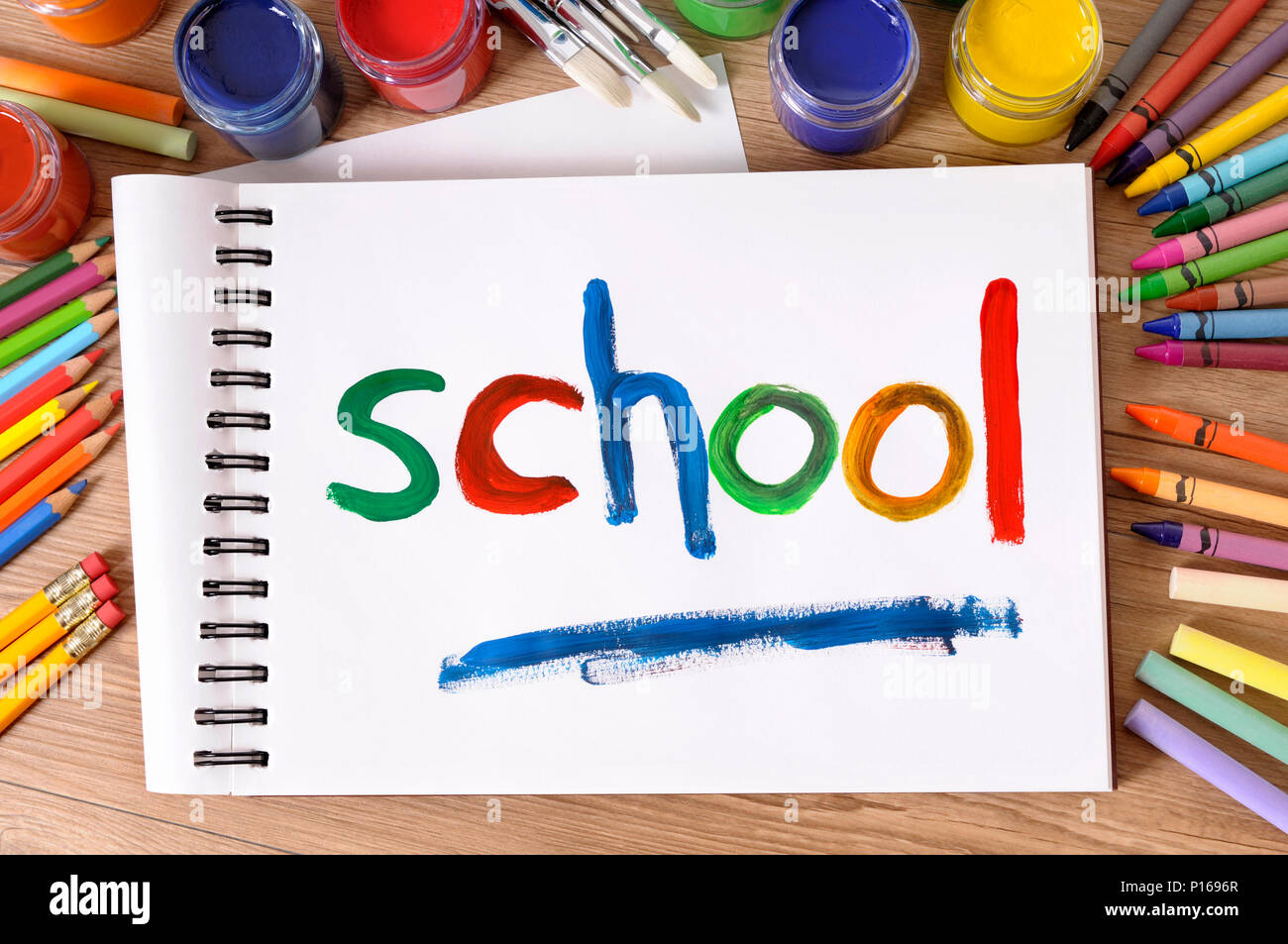 La scuola di parola dipinta su un bianco art book con vari colori, matite colorate e matite su un banco di scuola. Foto Stock