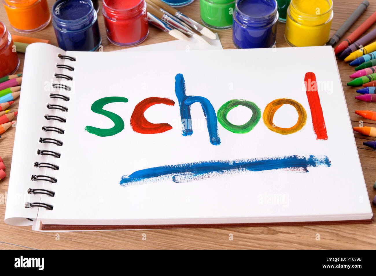 La scuola di parola dipinta su un bianco art book con vari colori, matite colorate e matite su un banco di scuola. Foto Stock