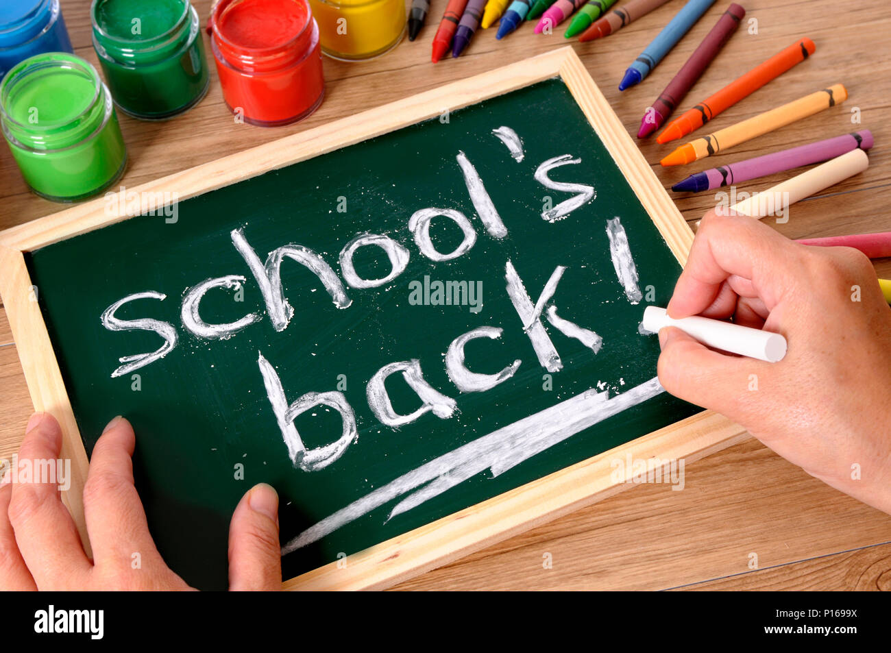 Le parole della scuola di ritorno essendo scritto su una piccola lavagna elementari con vari colori, matite colorate e matite su un banco di scuola. Foto Stock