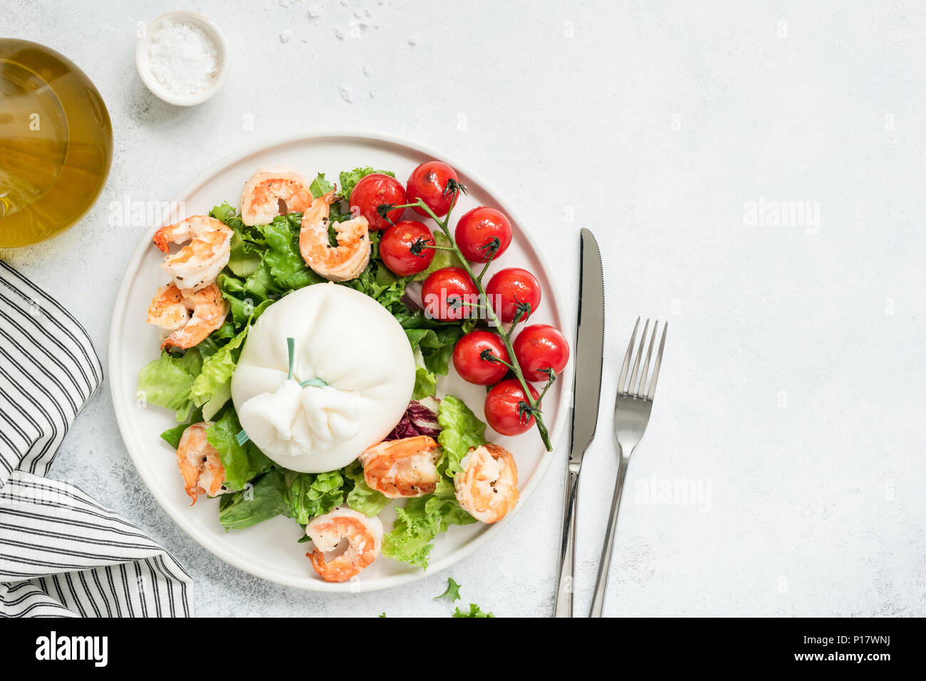 Una sana insalata con burrata, gamberi, pomodori e lattuga sulla piastra bianca. Vista superiore della gustosa insalata italiana con olio di oliva condimento. Mangiare sano concep Foto Stock
