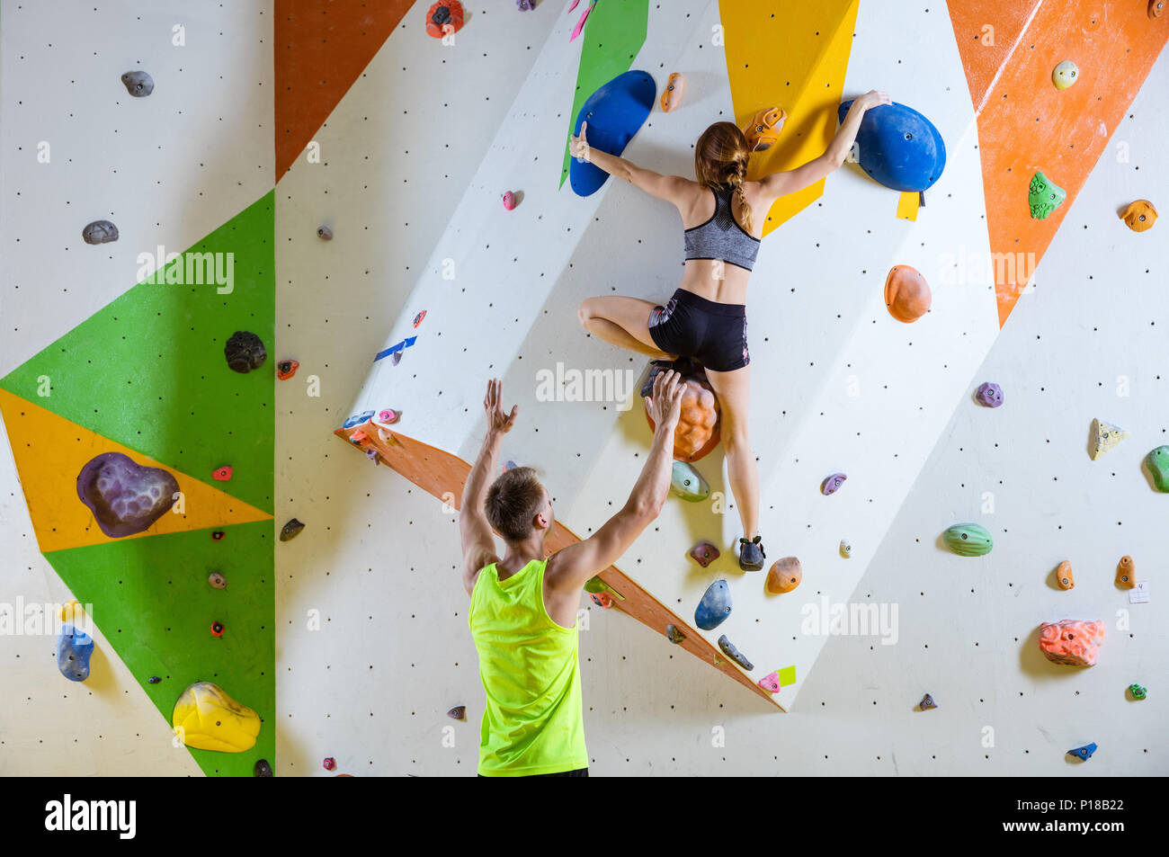 Arrampicatori in palestra di arrampicata. Giovane donna climbing bouldering problema (route), istruttore di sesso maschile che fissano la sua. Foto Stock
