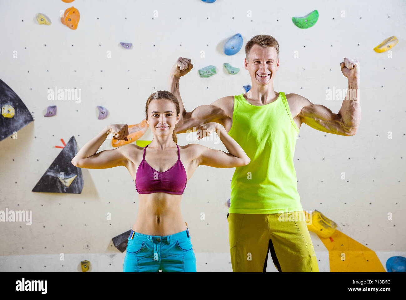 Giovani allegro maschi e femmine di arrampicatori flessione bicipite contro la parete di bouldering in palestra di arrampicata Foto Stock