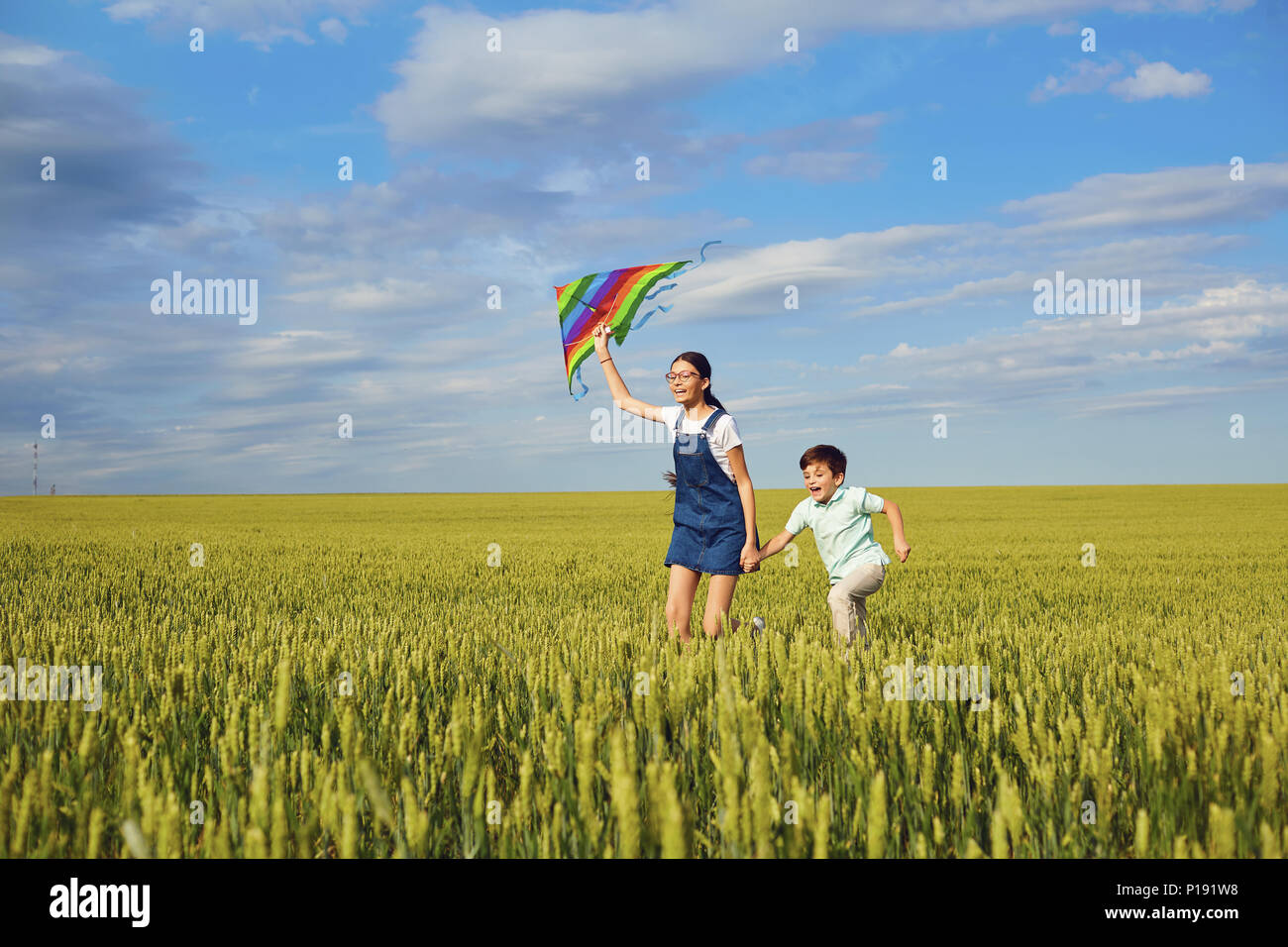 I bambini con un aquilone corrono attraverso il campo di grano in estate. Foto Stock