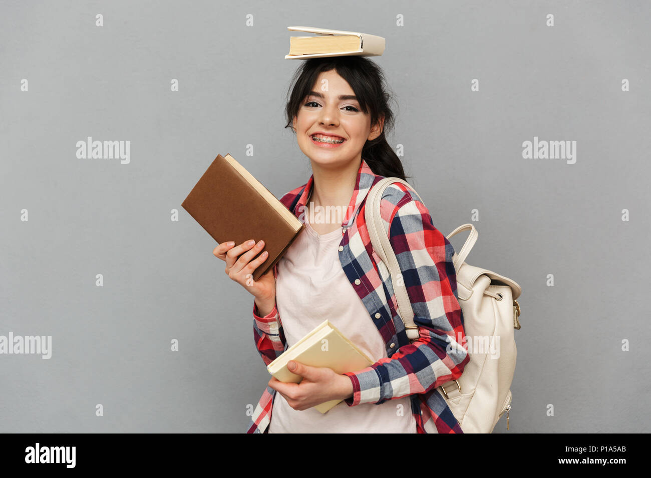 Immagine di felice signora giovane studente in piedi isolato su sfondo grigio parete libri di contenimento. Foto Stock