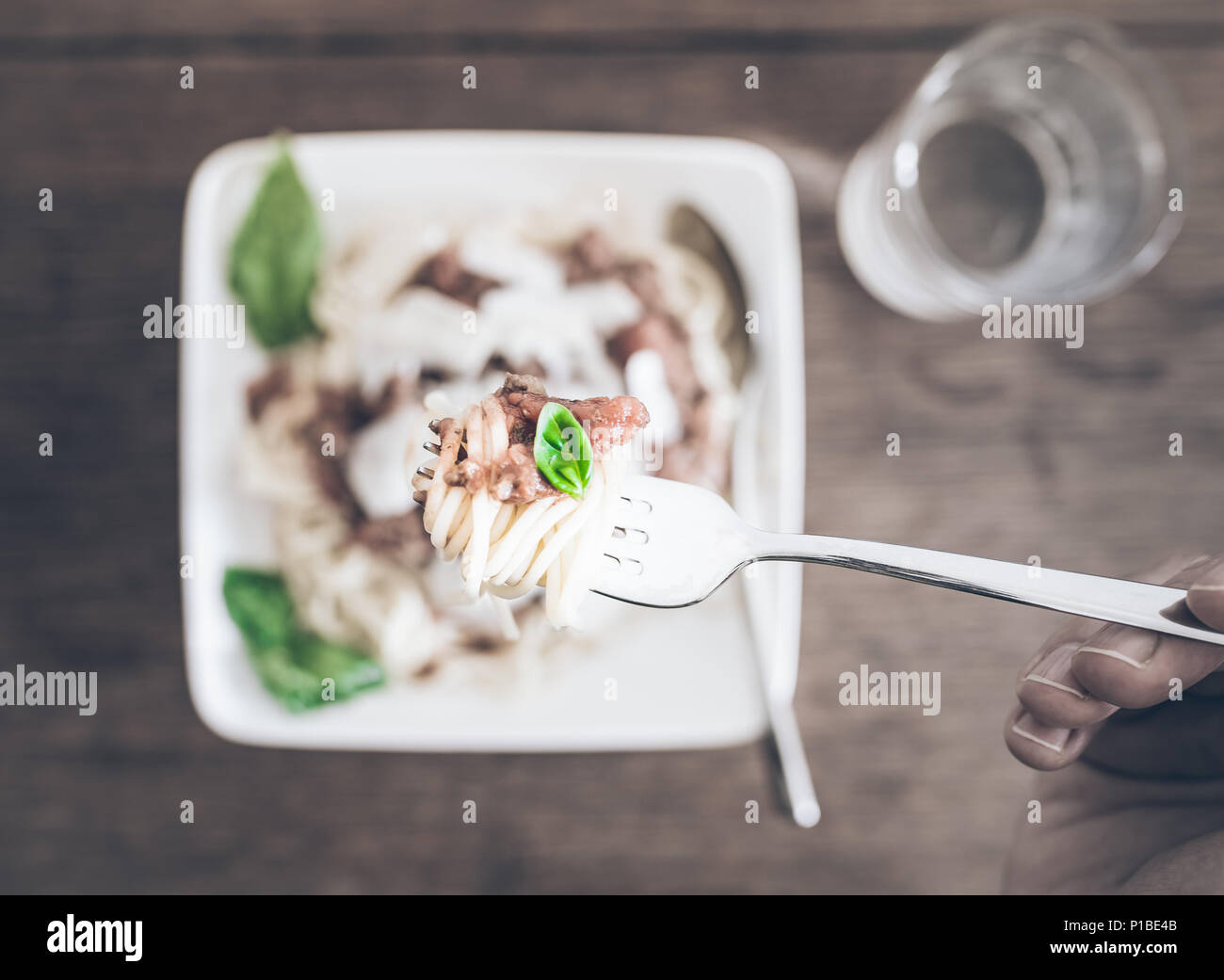 POV shot di persona a mangiare pasta con il ragù alla Bolognese contro la tavola in legno rustico Foto Stock