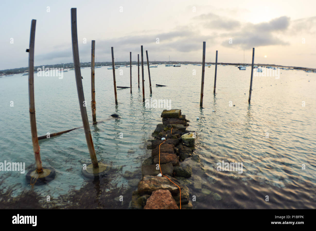 Piccolo molo, picchetti e barche ancorate in Estany des Peix marine laguna al tramonto nel Parco Naturale di Ses Salines (Formentera, isole Baleari, Spagna) Foto Stock