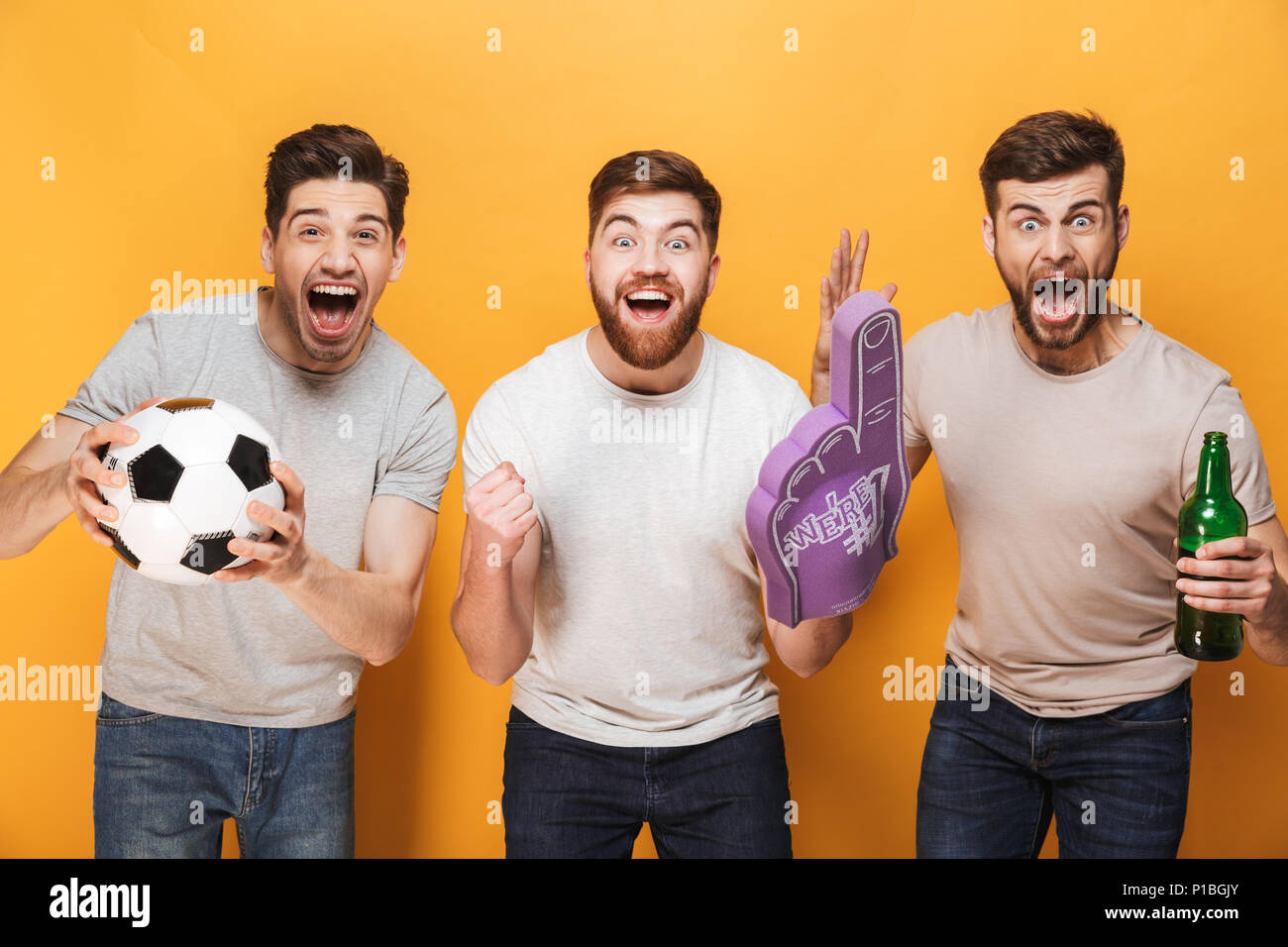 Tre giovani gioiosi uomini appassionati di calcio celebrano isolate su sfondo giallo Foto Stock