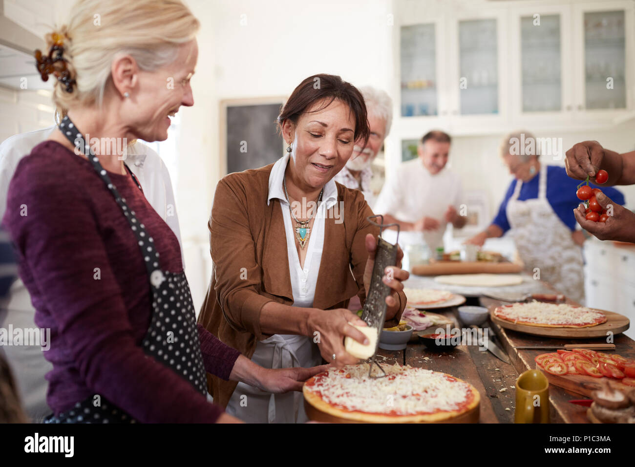 Le donne anziane amici grattugiare il formaggio sulla pizza in classe di cucina Foto Stock