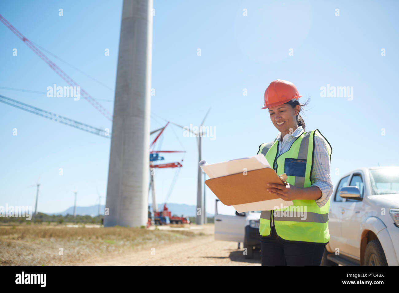 Sorridente ingegnere femmina con blueprint a sunny turbina eolica impianto di alimentazione Foto Stock