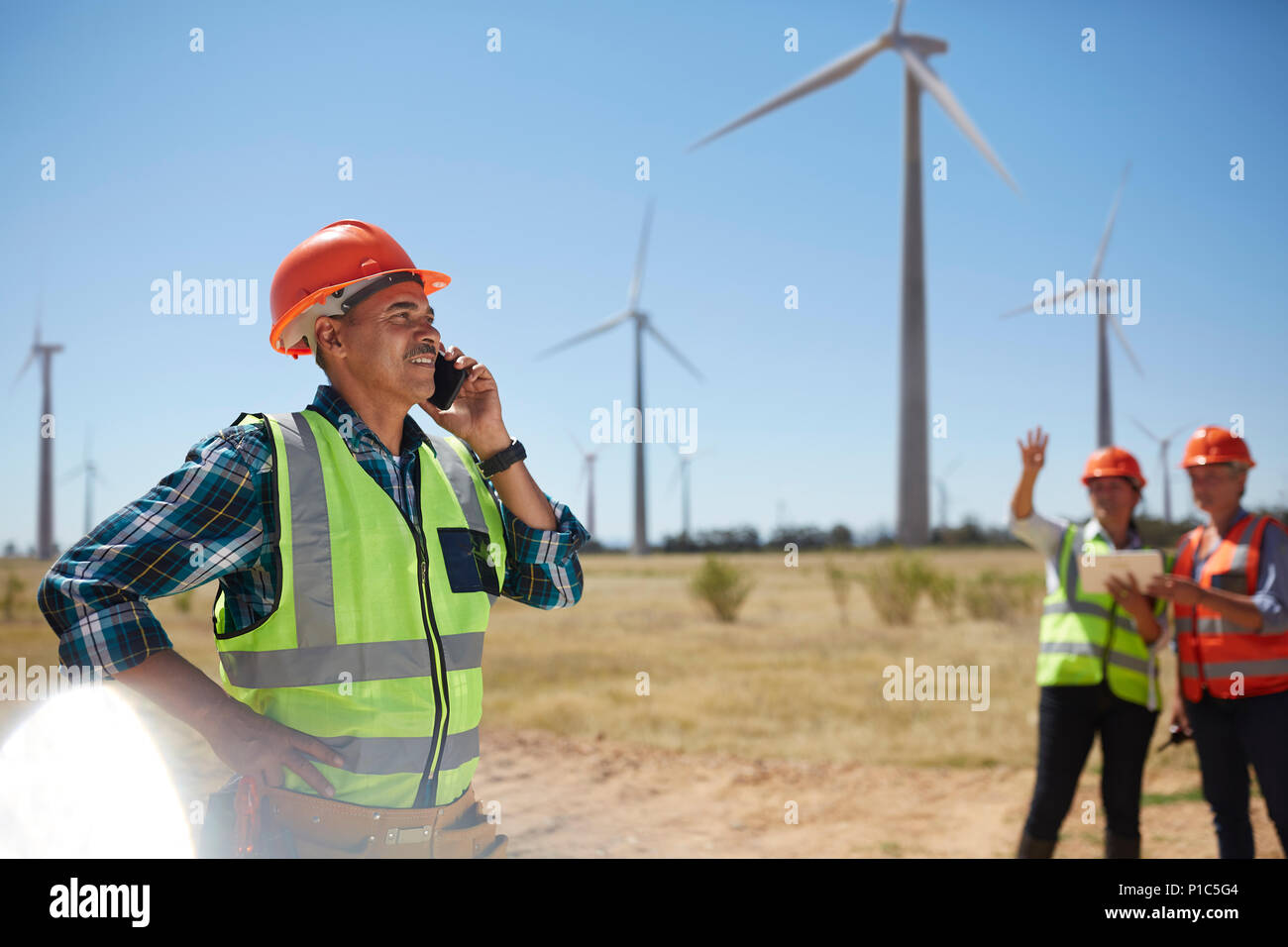 Ingegnere sorridente parlando al cellulare a sunny turbina eolica impianto di alimentazione Foto Stock