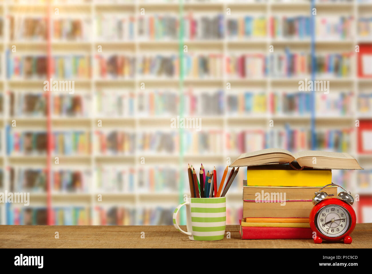 Immagine composita della pila di libri di tazza con matite colorate e sveglia sul tavolo di legno Foto Stock