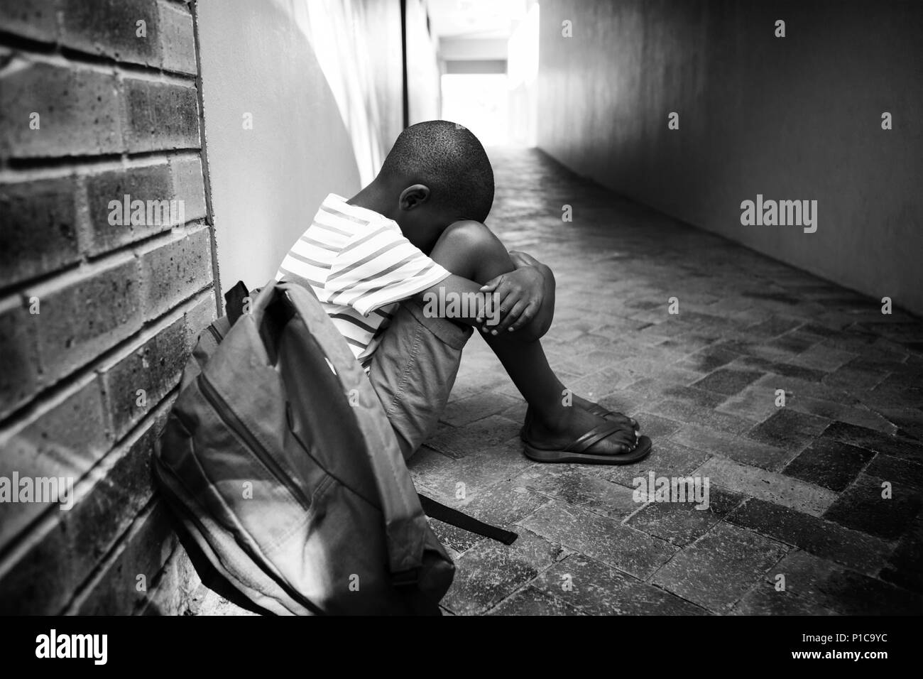 Ragazzo seduto da solo sul corridoio di scuola Foto Stock