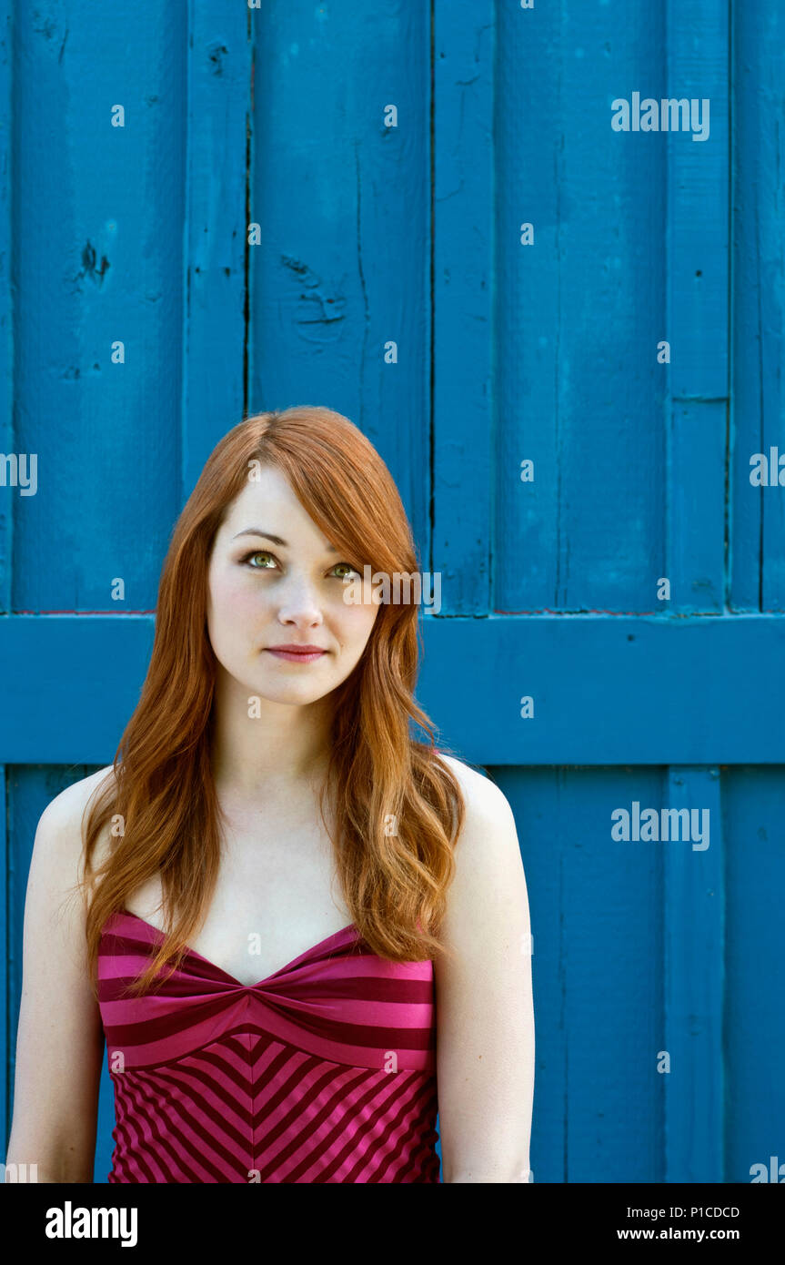 Una donna con i capelli rossi contro una parete blu Foto Stock
