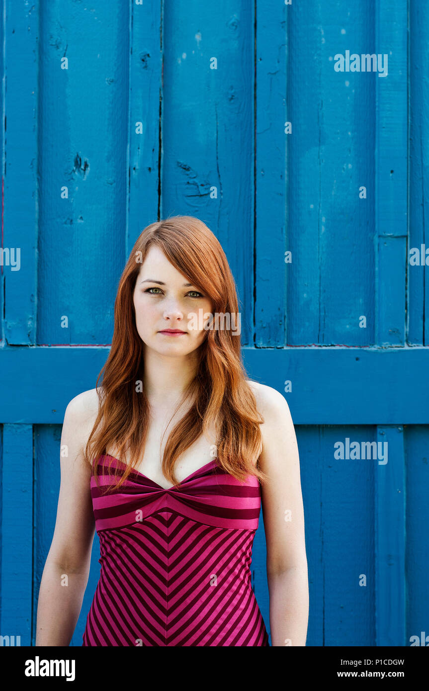 Una donna con i capelli rossi in piedi contro un muro di blu. Foto Stock