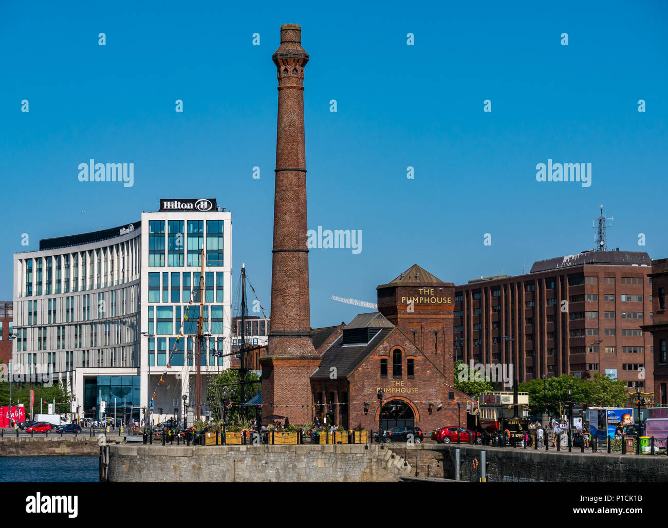 Albert Dock, Liverpool, in Inghilterra, Regno Unito, 11 giugno 2018. Regno Unito: meteo sole sul Mersey. Una bella giornata di sole con cielo azzurro lungo il fiume Mersey in Liverpool. La Pumphouse dockside pub con gente seduta al di fuori e la sua torre in mattoni con il moderno Hilton Hotel in background Foto Stock