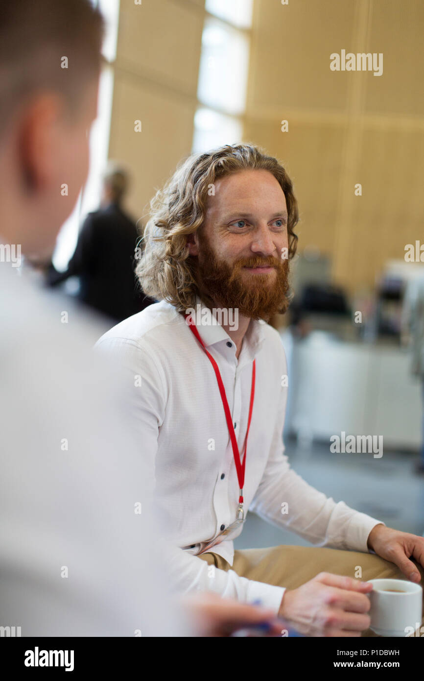 Imprenditore sorridente di bere il caffè a una conferenza Foto Stock