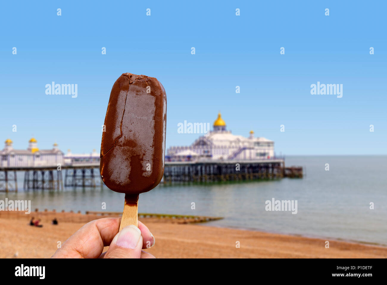 Mano che tiene un choc per lecca-lecca di ghiaccio in riva al mare Foto Stock