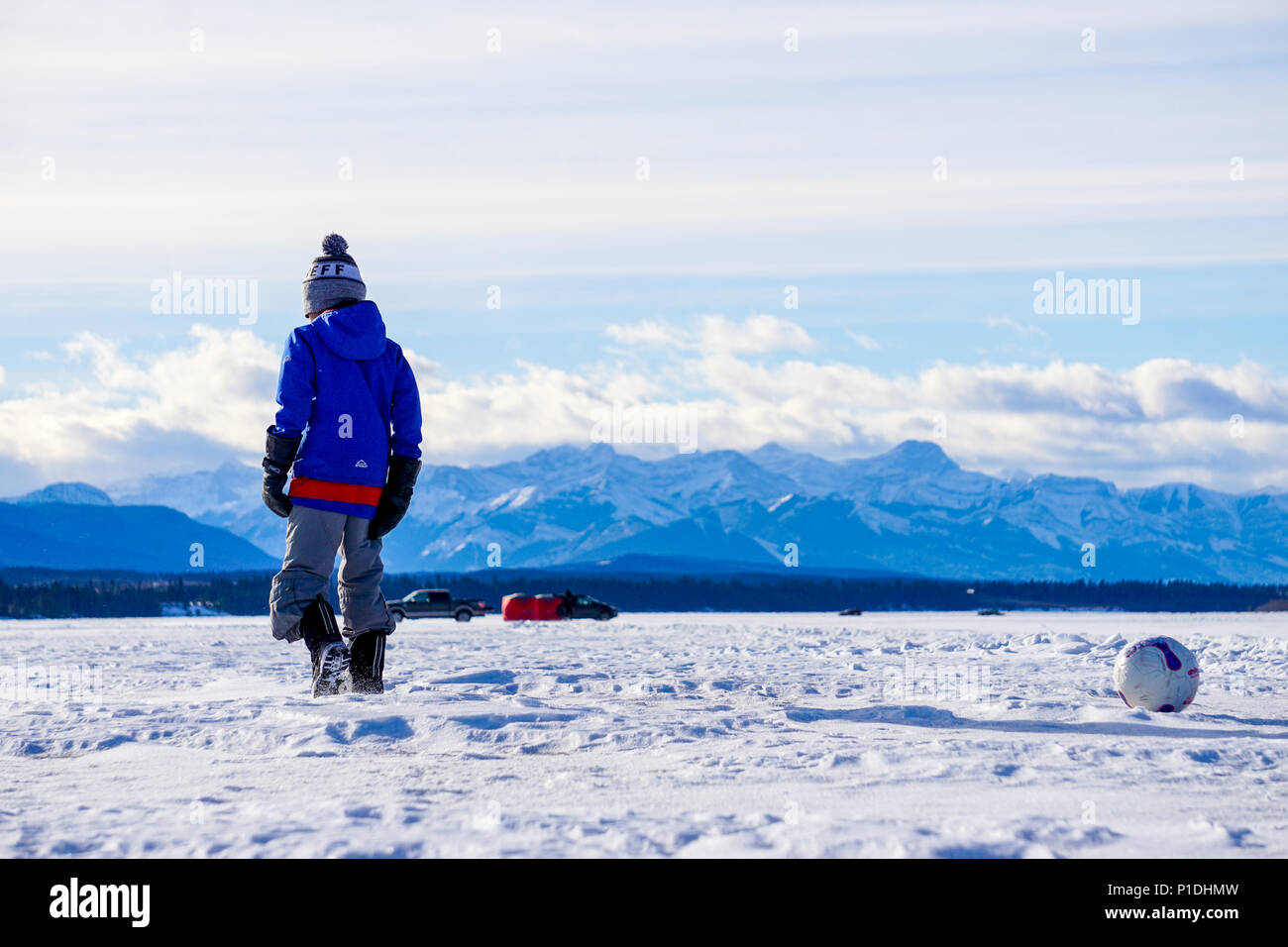 Bambino a piedi dal calcio su un lago ghiacciato non lontano dalle montagne di Banff. Foto Stock