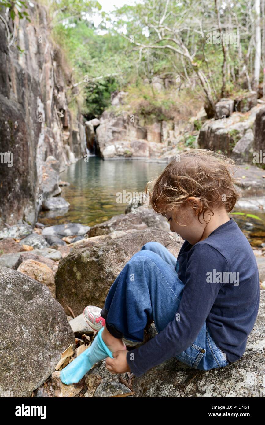 Ragazza giovane mettendo sul suo calzini e scarpe in un ambiente naturale, Paluma Range National Park, Rollingstone QLD, Australia Foto Stock