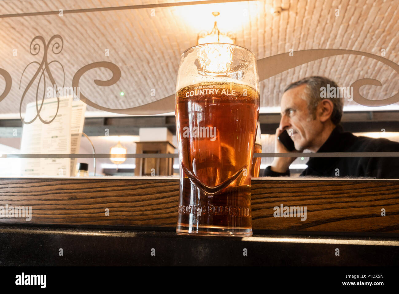 Uomo maturo con una pinta di birra artigianale parlando al telefono cellulare in JD Wetherspoon pub in Inghilterra. Regno Unito Foto Stock