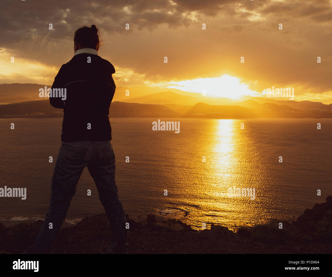 Vista posteriore della donna che guarda sul mare dalle alte scogliere al tramonto. Femmina salute mentale/depressione, malattia mentale,solitudine...,il concetto di immagine Foto Stock
