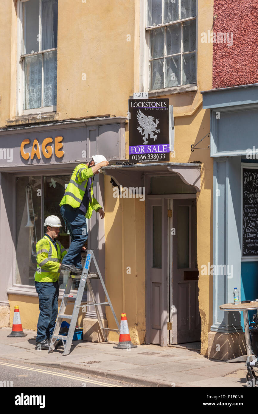 Due BT openreach ingegneri lavorano su un shopfront a Malmesbury High Street, Wiltshire, Regno Unito Foto Stock