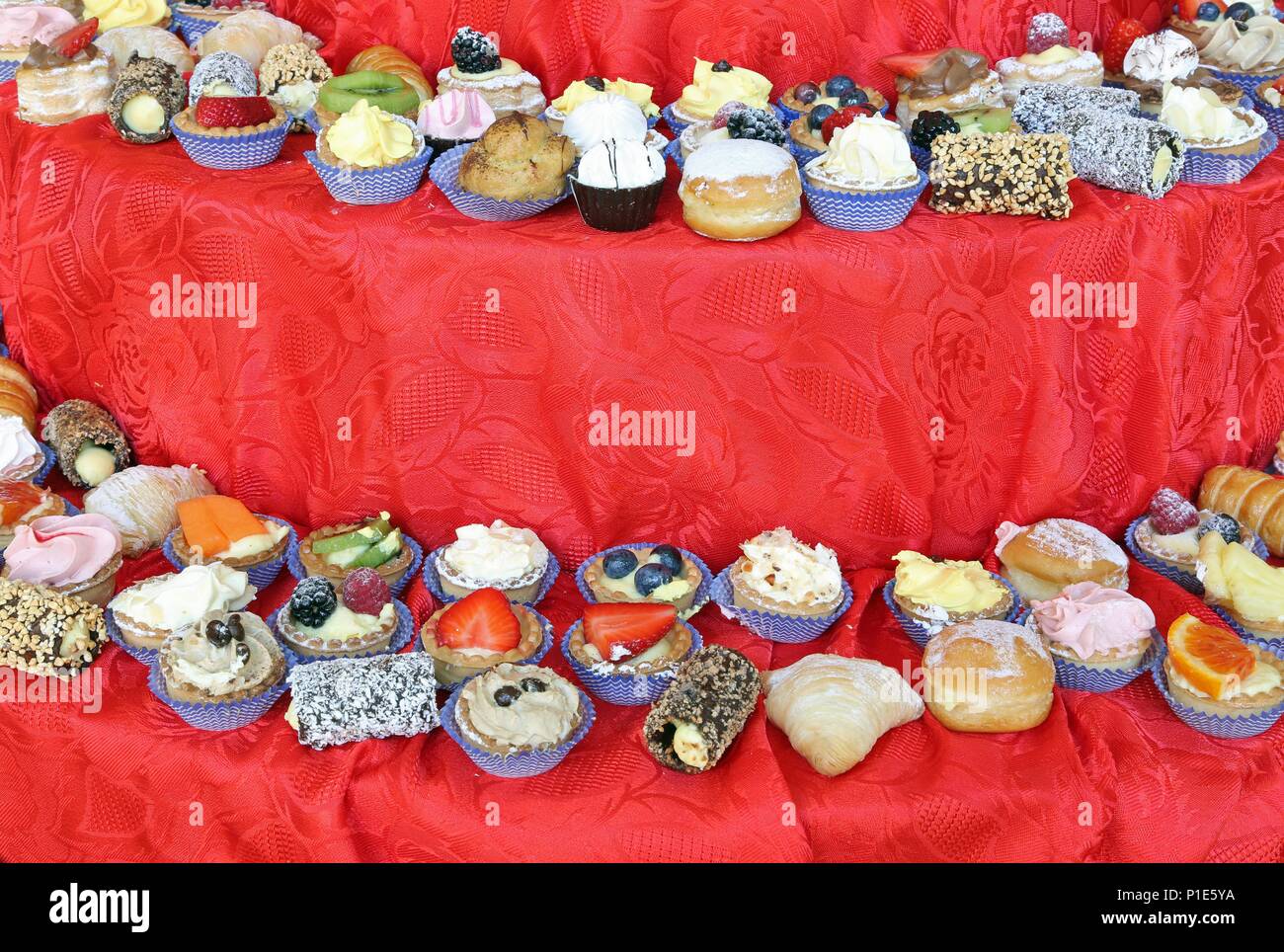 Abbondanza di paste dolci sulla sommità della tovaglia rossa durante il ricevimento di nozze Foto Stock