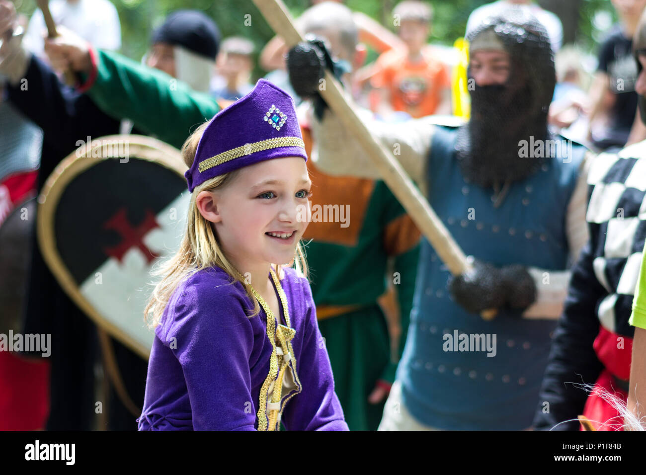 Nis, Serbia - Giugno 10, 2018: Medievale piccola principessa in abito viola e cavalieri con arma in aria in sfondo sfocato. Medioevo festival Foto Stock