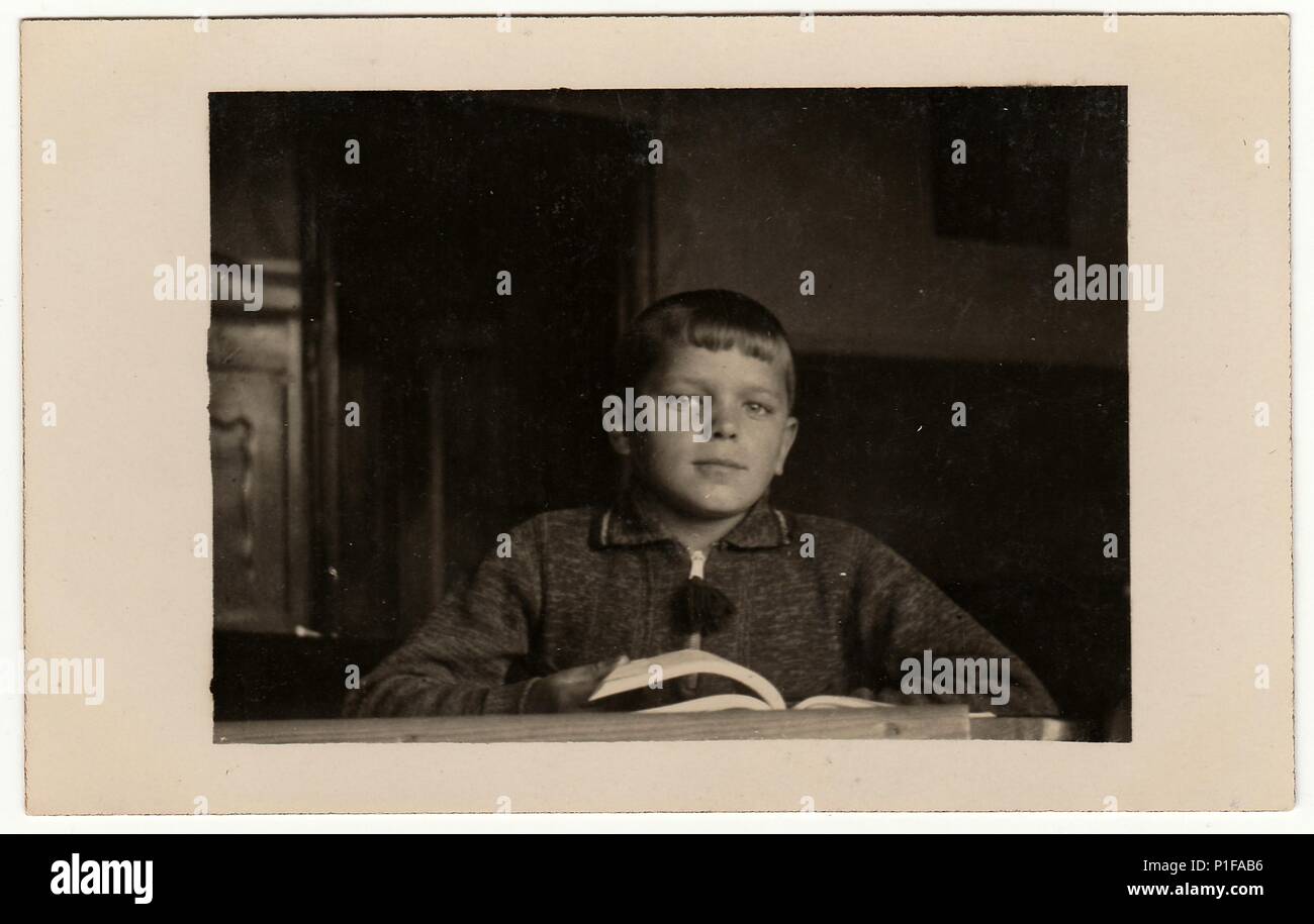 EILENBURG, GERMANIA - CIRCA 1950s: Foto d'epoca mostra il ragazzo con libro alla scrivania. Foto retrò in bianco e nero. 1950s. Foto Stock