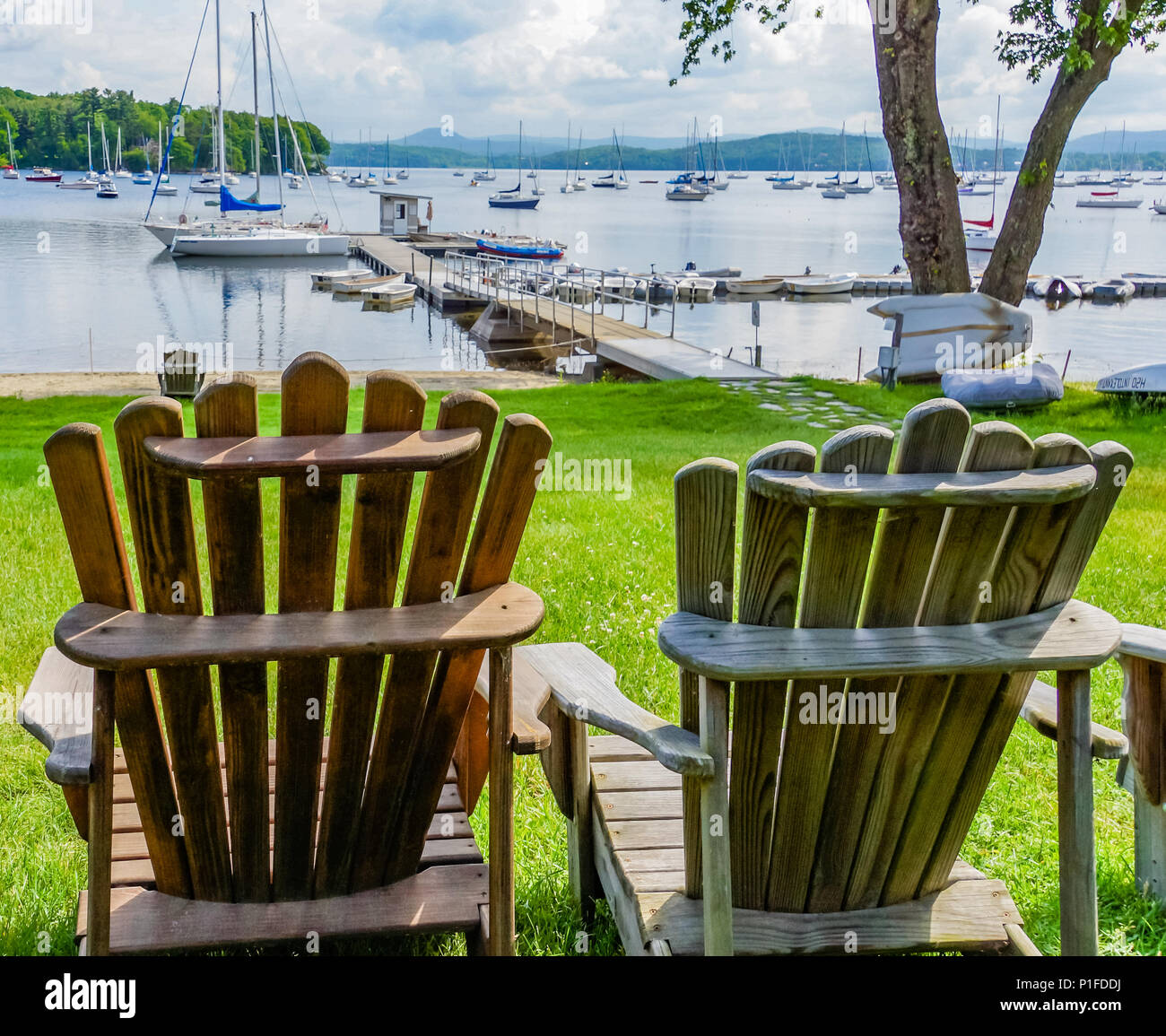 Due di legno sedie di Adirondack con una vista del lago con molte barche a vela ormeggiata Foto Stock