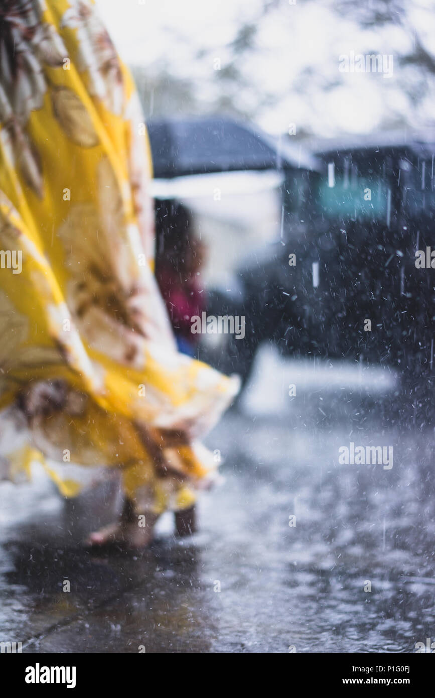 Donna con abito giallo a piedi sotto la pioggia Foto Stock
