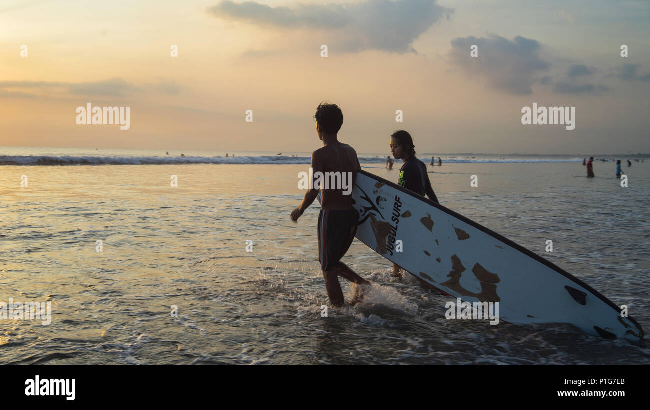 Una coppia porta surfista-board sulla spiaggia in Kuta Bali Indonesia Foto Stock