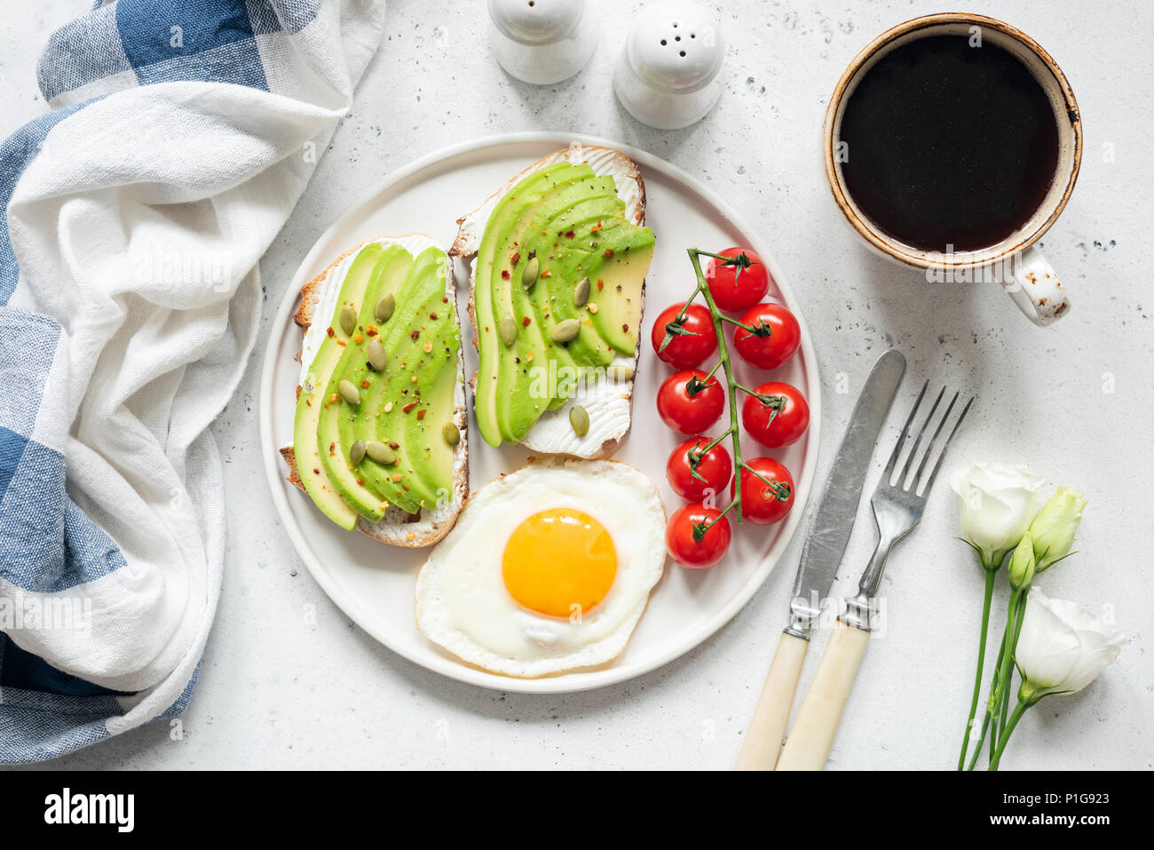 La colazione avocado toast con uovo fritto, pomodori ciliegini, una tazza di caffè e fiori bianchi. La prima colazione a letto. Uno stile di vita sano, mangiare sano concetto Foto Stock