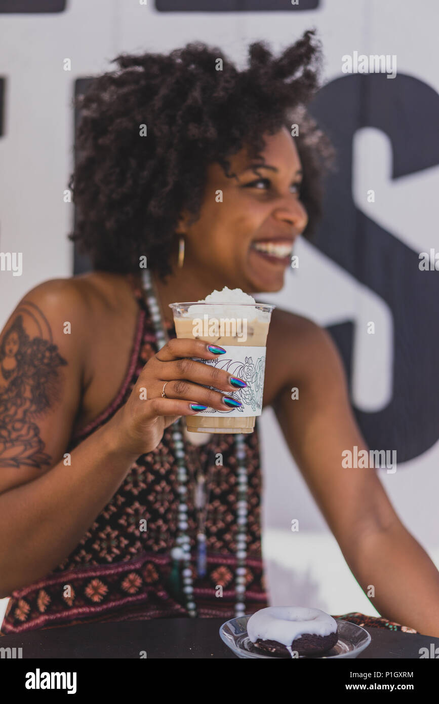 Un elegante nero donna a bere caffè e sorridente Foto Stock